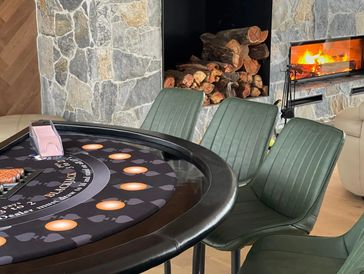 Poker table with green chairs near a fireplace.