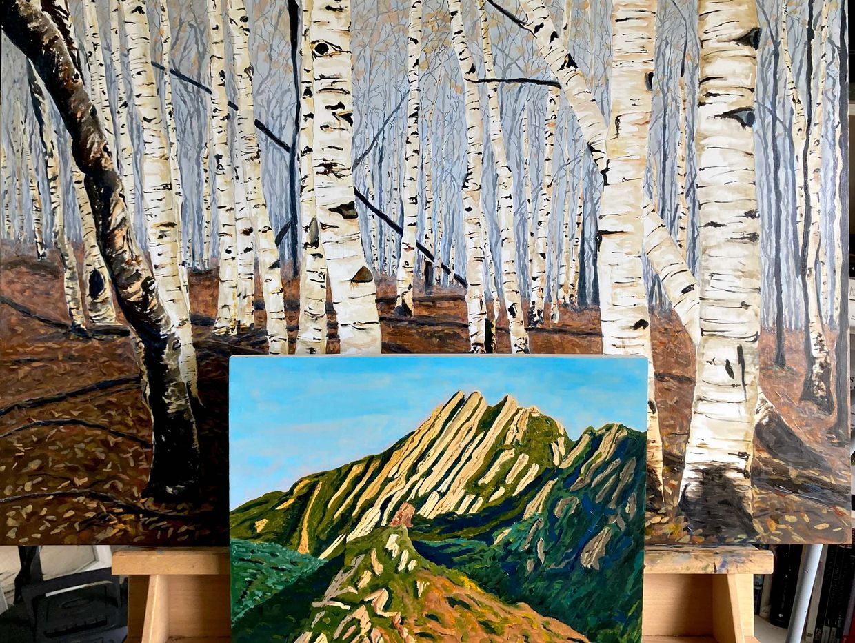 two paintings on an easel, landscape of mountains in front, landscape of aspen forest larger in back