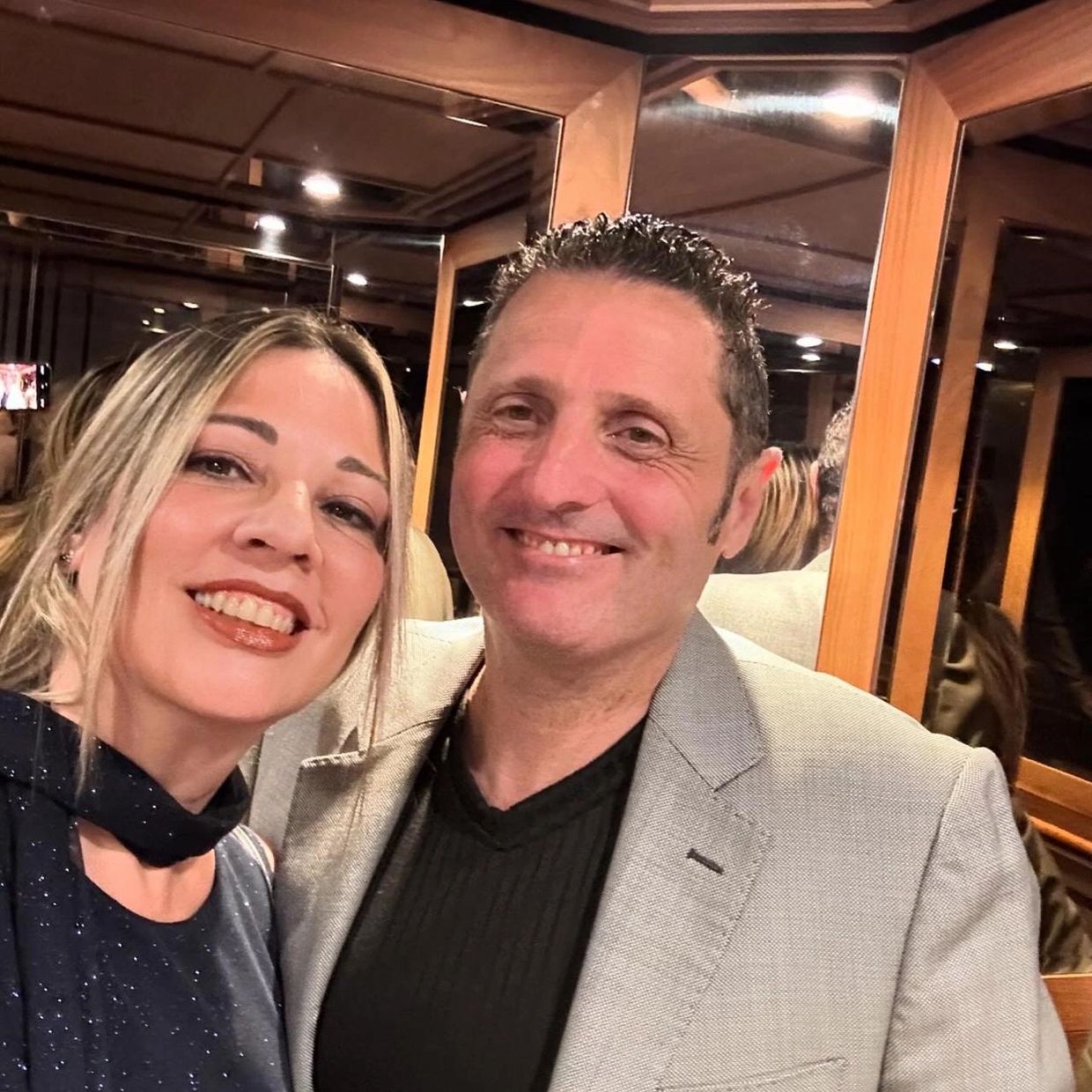 Smiling couple posing for a selfie in a room with wooden paneling and mirrors.