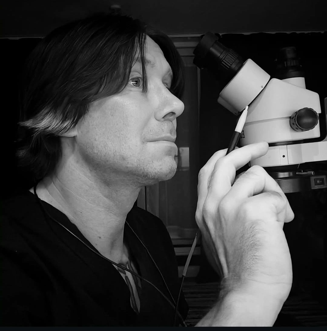 Man examining something through a microscope in a black and white photo.