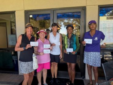 Five women standing and holding cards, smiling outdoors.