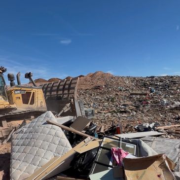 Bulldozer moving trash at a large landfill under clear blue sky.