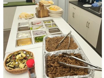 Buffet setup with meat, toppings, condiments, and plates in a kitchen.