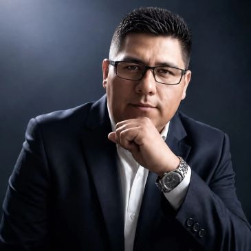 Hombre con gafas y traje oscuro en pose pensativa.
