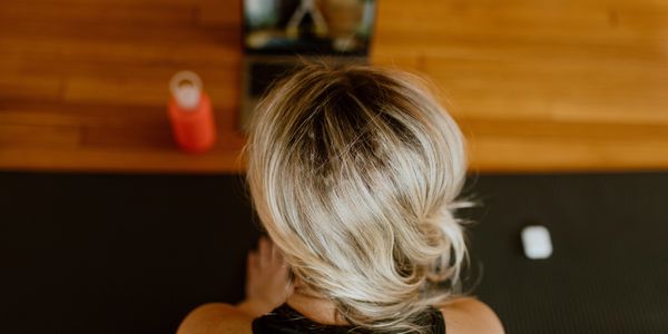 Woman with blonde hair doing yoga with a laptop and water bottle nearby.