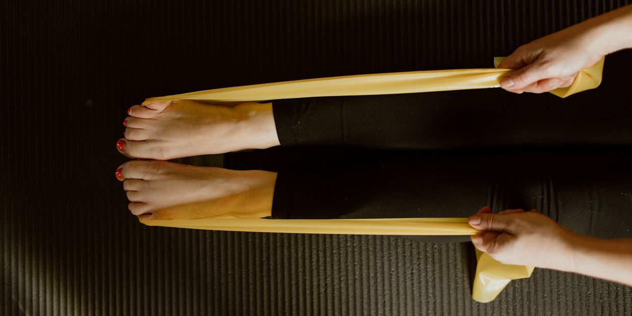 Person stretching feet with a yellow resistance band on a black mat.