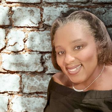 Smiling woman in black top poses against a textured brick wall.