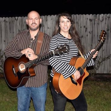 man and woman smiling, each holding an acoustic guitar in an outdoor setting