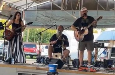 3 musicians playing on stage. Two acoustic guitars and a drummer