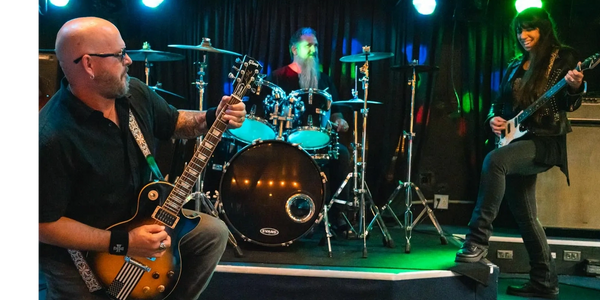 Three musicians performing energetically on stage one playing drums and the other two playing guitar