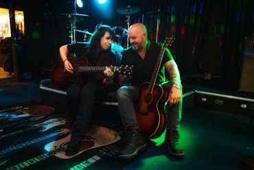 Woman and man sitting on stage with two acoustic guitars looking at each other