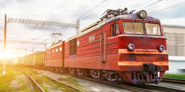 A red freight train speeding on railway tracks during sunset.