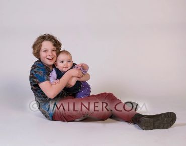 Smiling boy holding a baby in a studio setting.