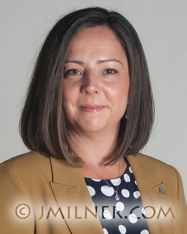 Professional woman with shoulder-length hair in a mustard blazer and polka dot blouse.