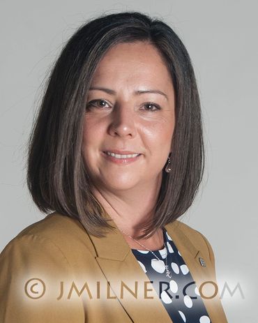 Professional headshot of a woman with straight shoulder-length hair, wearing a mustard blazer.