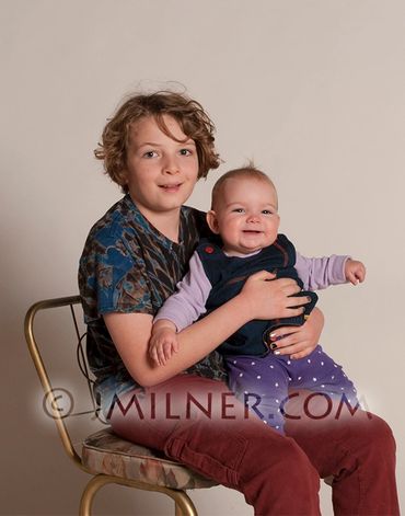 Young boy sitting on chair holding a smiling baby girl.