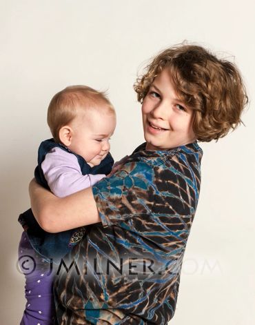 Young boy happily holding a baby girl in his arms.