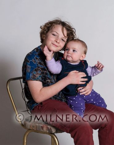 Young child lovingly holding a baby on a chair against a plain background.