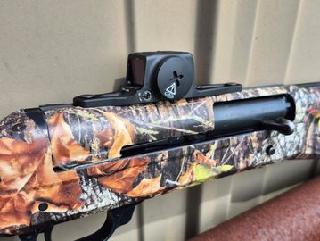 Close-up of a camouflaged shotgun with a red dot sight.