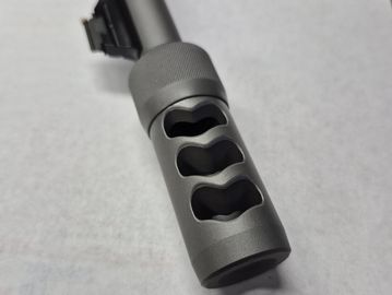 Close-up of a gray metal firearm muzzle brake with three vent holes.