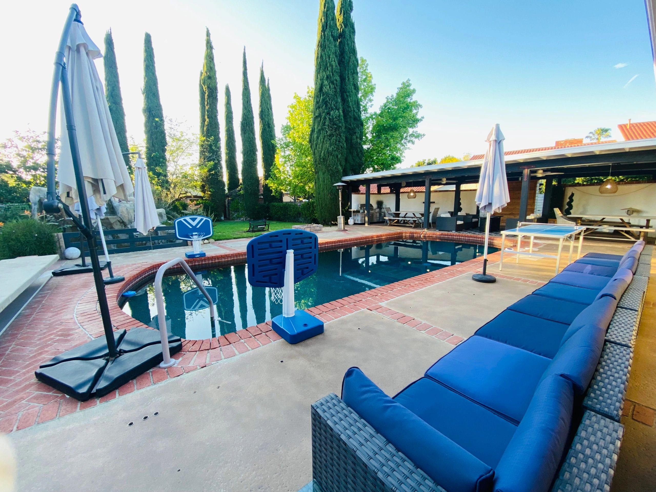 A backyard pool area with blue cushioned seating and basketball hoops.