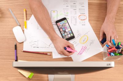 Overhead view of person writing on papers with phone, computer, mouse and pens