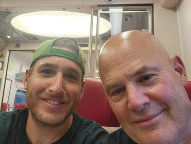 Two men smiling for a selfie inside a vehicle.