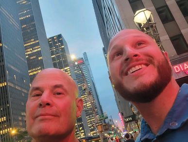 Two men smiling in a city at dusk.