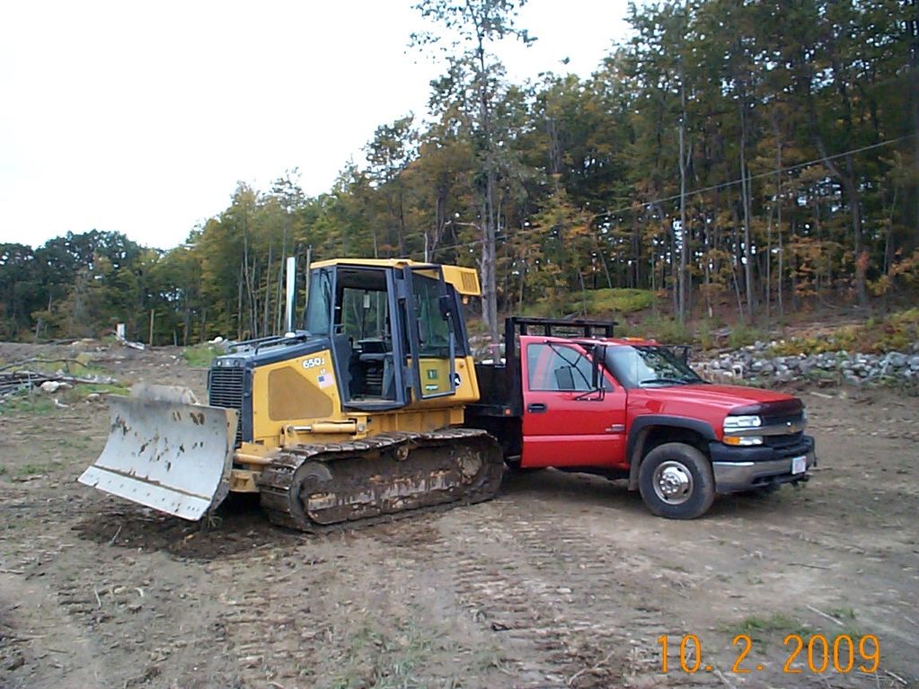 Yellow bulldozer parked next to a red pickup truck on a dirt clearing.