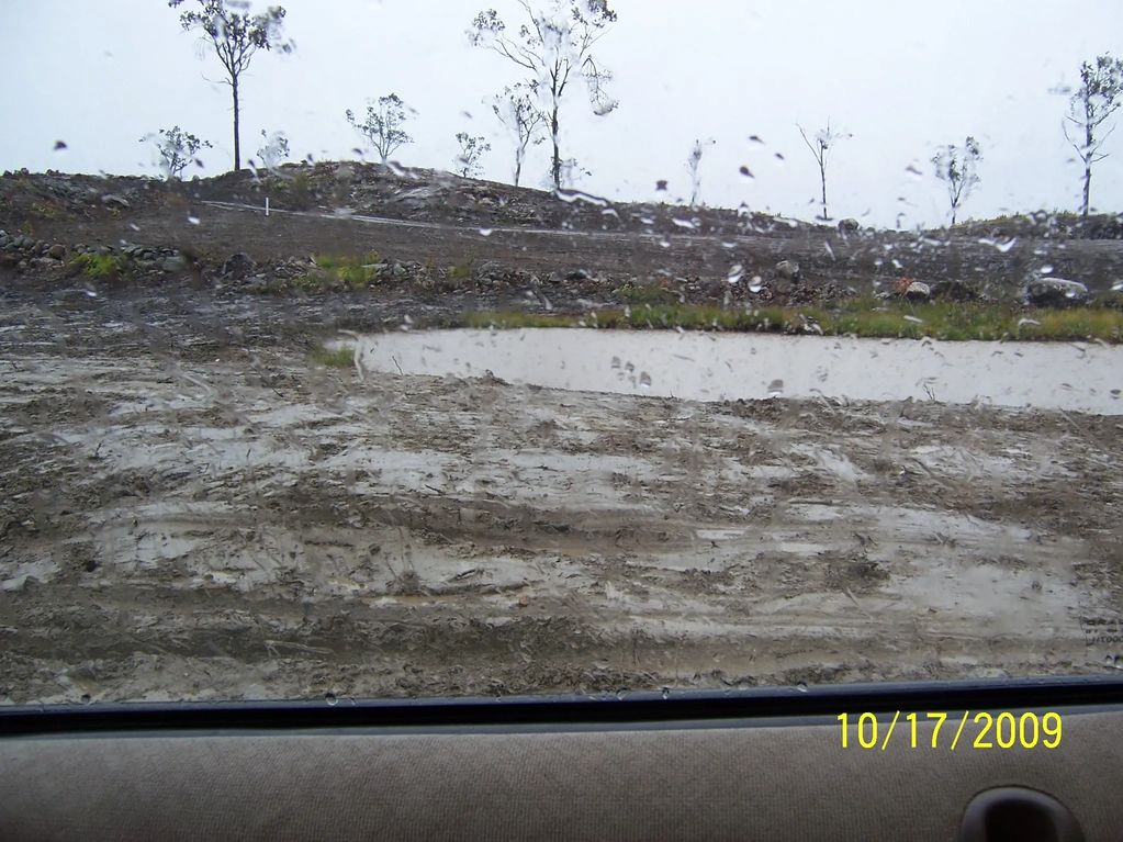View of a muddy, rainy landscape with sparse trees from inside a car.