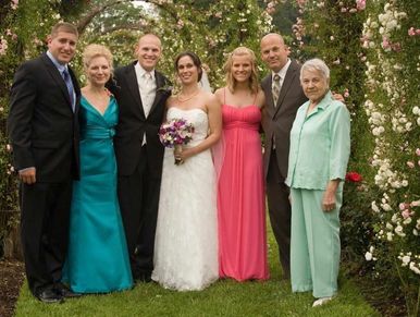 A wedding group photo with six people under a flower arch.