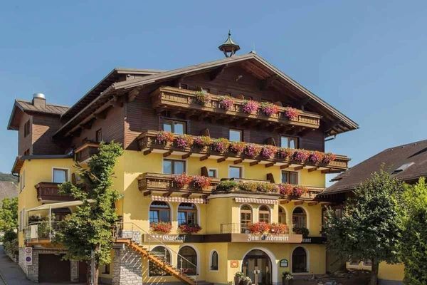 A charming multi-story alpine building with flower-filled balconies under a clear blue sky.