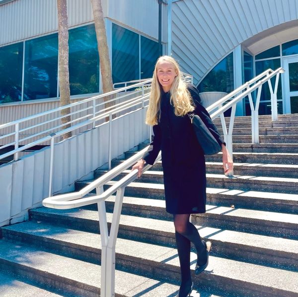 Smiling woman in black dress on stairs outside a modern building.