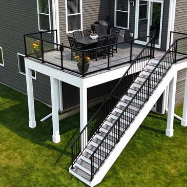 Modern elevated deck with black railing and stairs overlooking a green lawn.