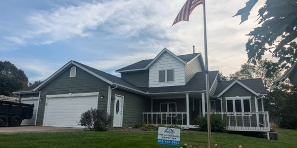 Suburban house with American flag and real estate sign on lawn.