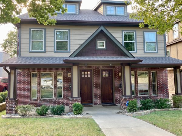 Duplex house with red brick and beige siding, featuring two wooden front doors and a small garden.  