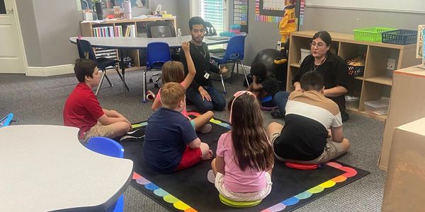 Children and teachers sitting in a classroom circle.