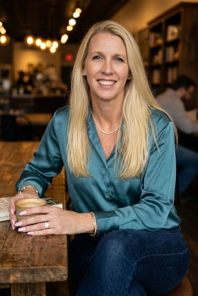 Woman in teal blouse holding coffee cup at wooden table.