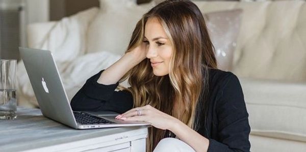 Mujer con laptop sentada en el suelo junto a una mesa.