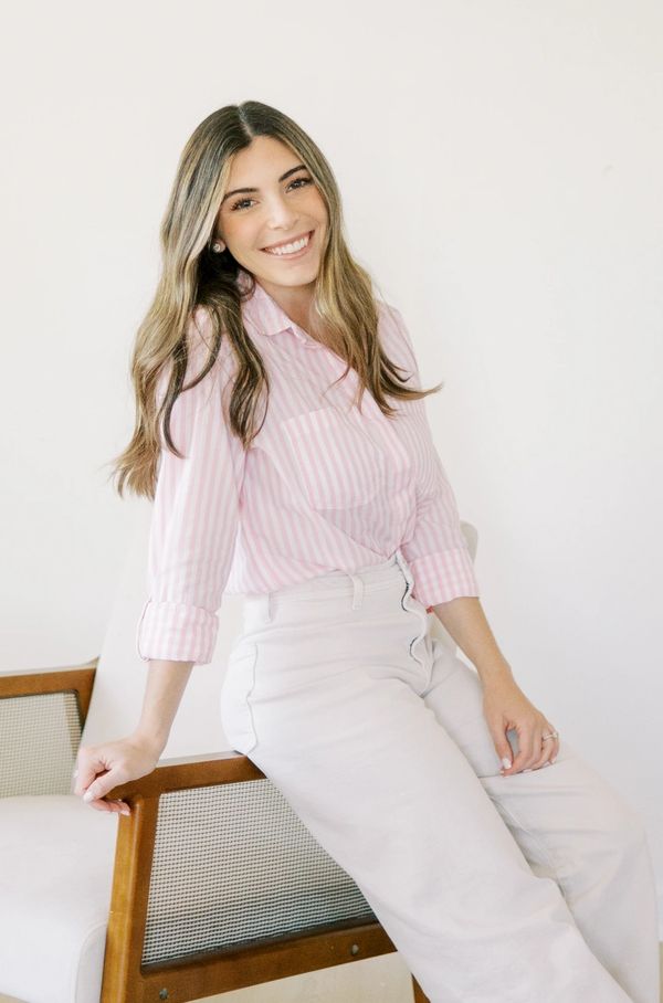 Smiling woman in pink striped shirt sitting on chair.