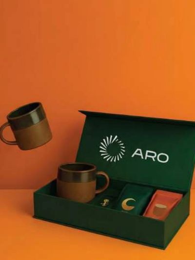 طقم هدايا أنيق للقهوة يتضمن أكواباً بنية اللون وأكياس قهوة متنوعة في علبة خضراء.