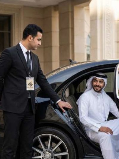 سائق محترف يساعد راكباً على الصعود إلى سيارة سوداء فاخرة، يمثل خدمات تأجير السيارات الفاخرة وخدمات نقل الشخصيات المهمة.