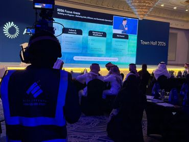 جمهور فعالية الشركات يشاهد منصة LED كبيرة مزودة بصور تحمل العلامة التجارية، بينما يقوم مصور محترف بالتقاط صور للحدث، وعرض أعمال معرض Rizq Events وإنتاج الفعاليات.