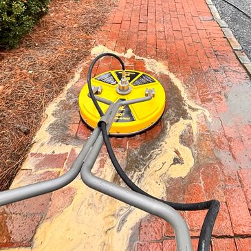 A yellow surface cleaner cleaning a wet brick pathway outdoors.