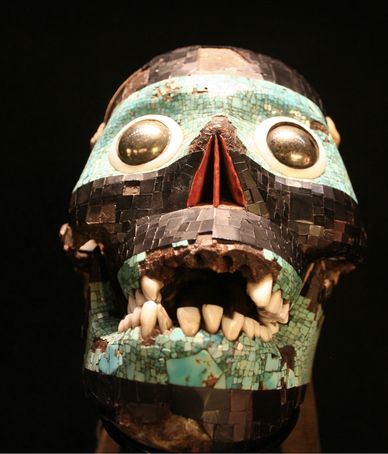 Ancient mosaic skull with turquoise and shell inlays and prominent teeth.