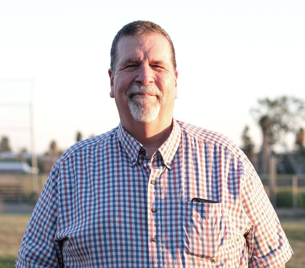Smiling man in a plaid shirt outdoors.