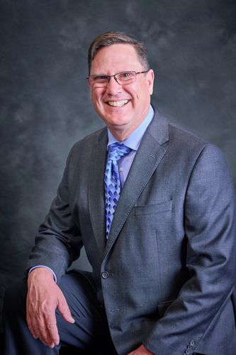Smiling man in a suit and glasses poses against a dark background.