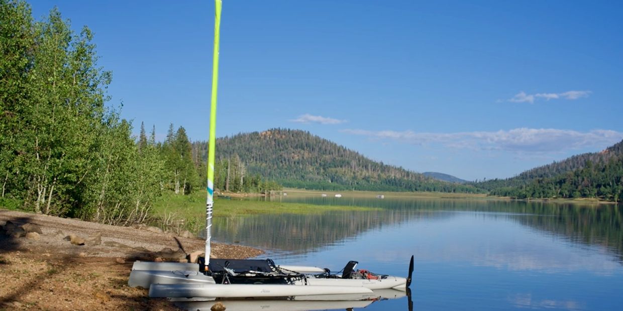 A small sailboat docked on a calm lake with forested hills in the background.