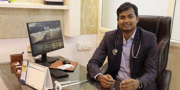 A doctor sitting at his desk with a stethoscope, smiling at the camera.