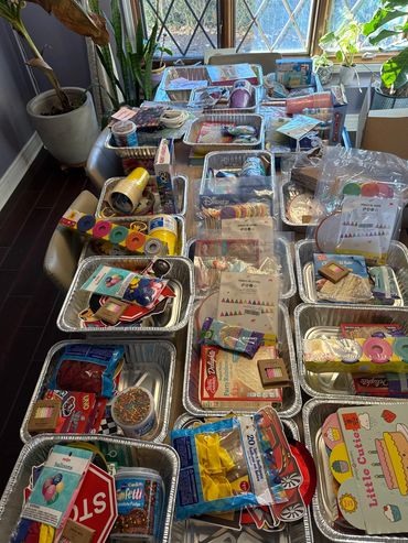 Multiple aluminum trays filled with assorted craft supplies and party items.